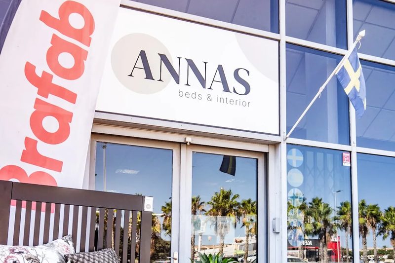 Entrén till Annas beds & interior i Torrevieja, med butikens skylt över dörren, en svensk flagga och en bäddad säng utställd på trottoaren.