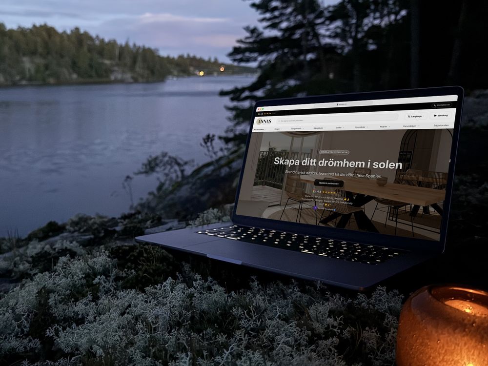 annas.cc öppen i en bärbar dator på en lavklädd klippa vid vattnet i skymningen, med en tänd lykta bredvid.
