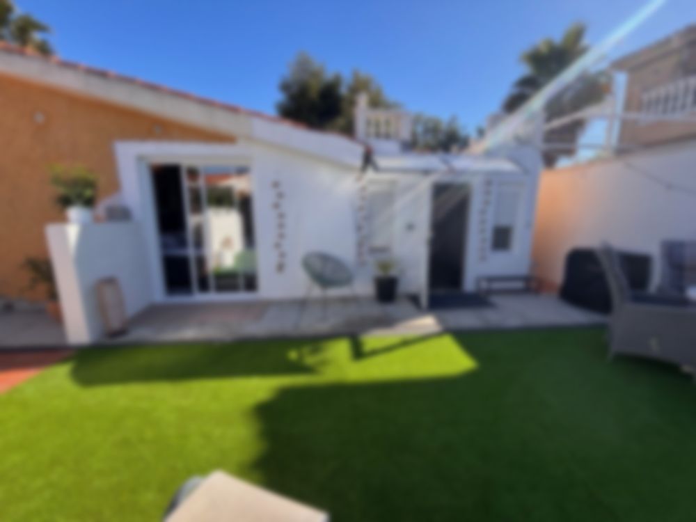 Sviten i Torrevieja med gräsmatta, vit fasad och palmer i solsken, suddig i bakgrunden.